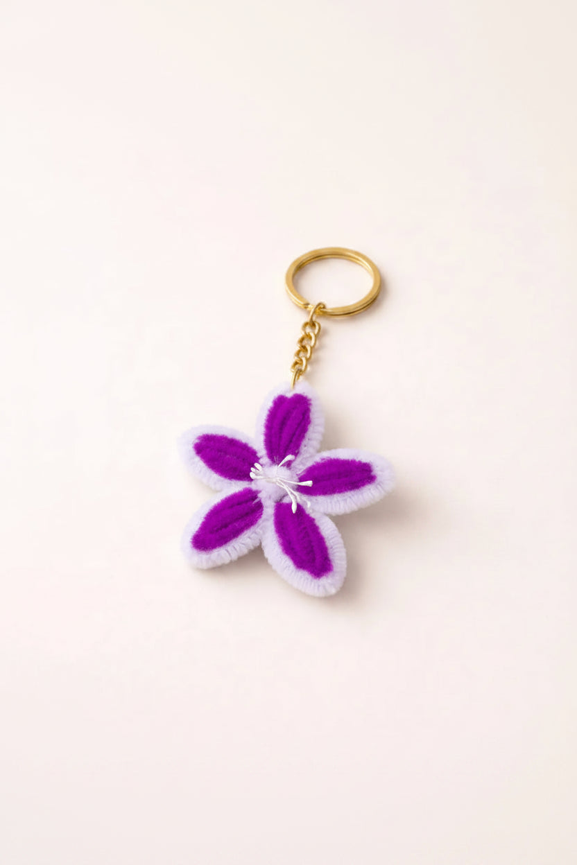 Handmade purple and white flower keychain made with pipe cleaners with gold ring on soft neutral background aesthetic product photo