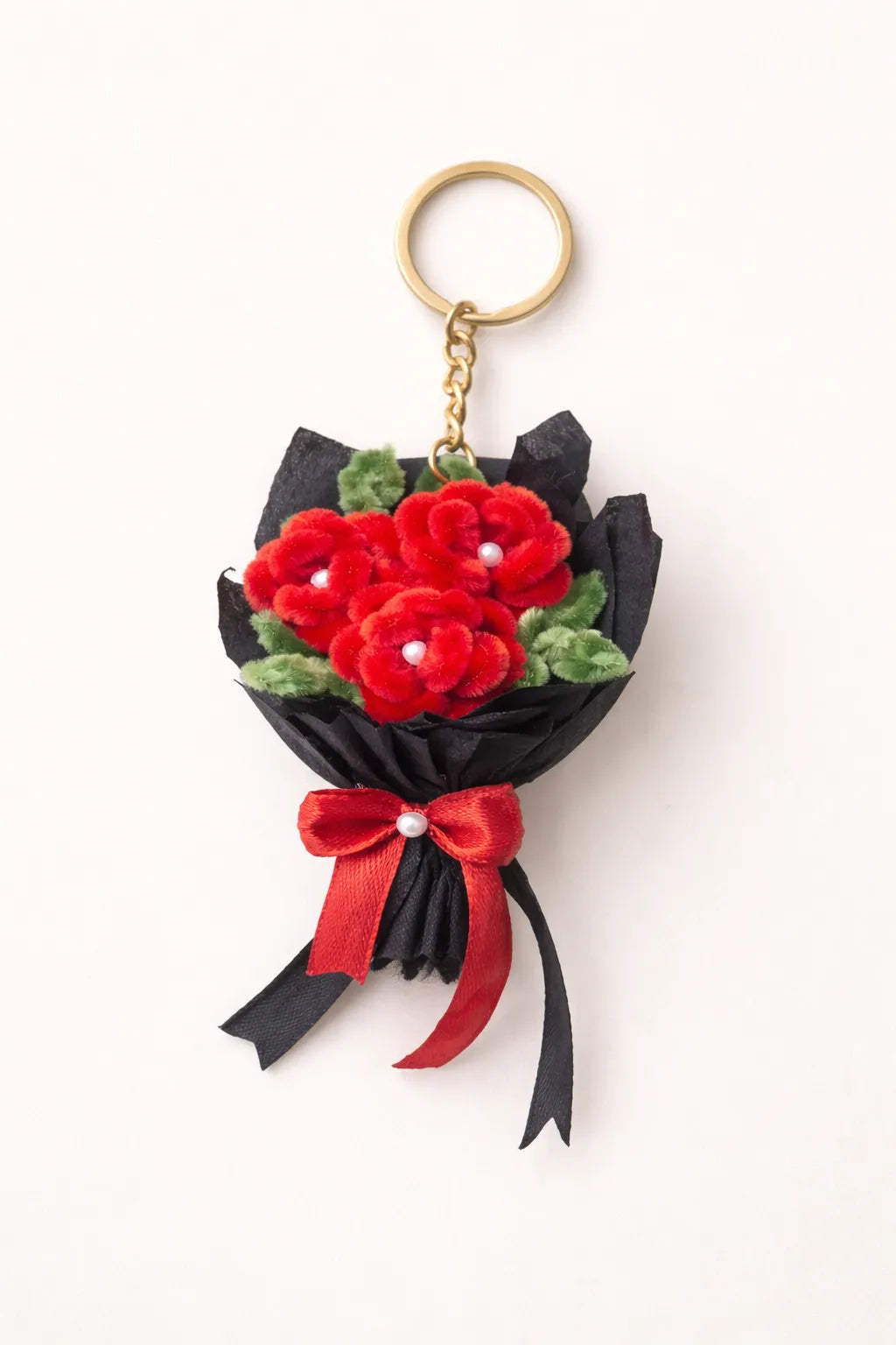 Handmade mini red rose bouquet keychain made with pipe cleaners wrapped in black paper with red ribbon bow on soft neutral background