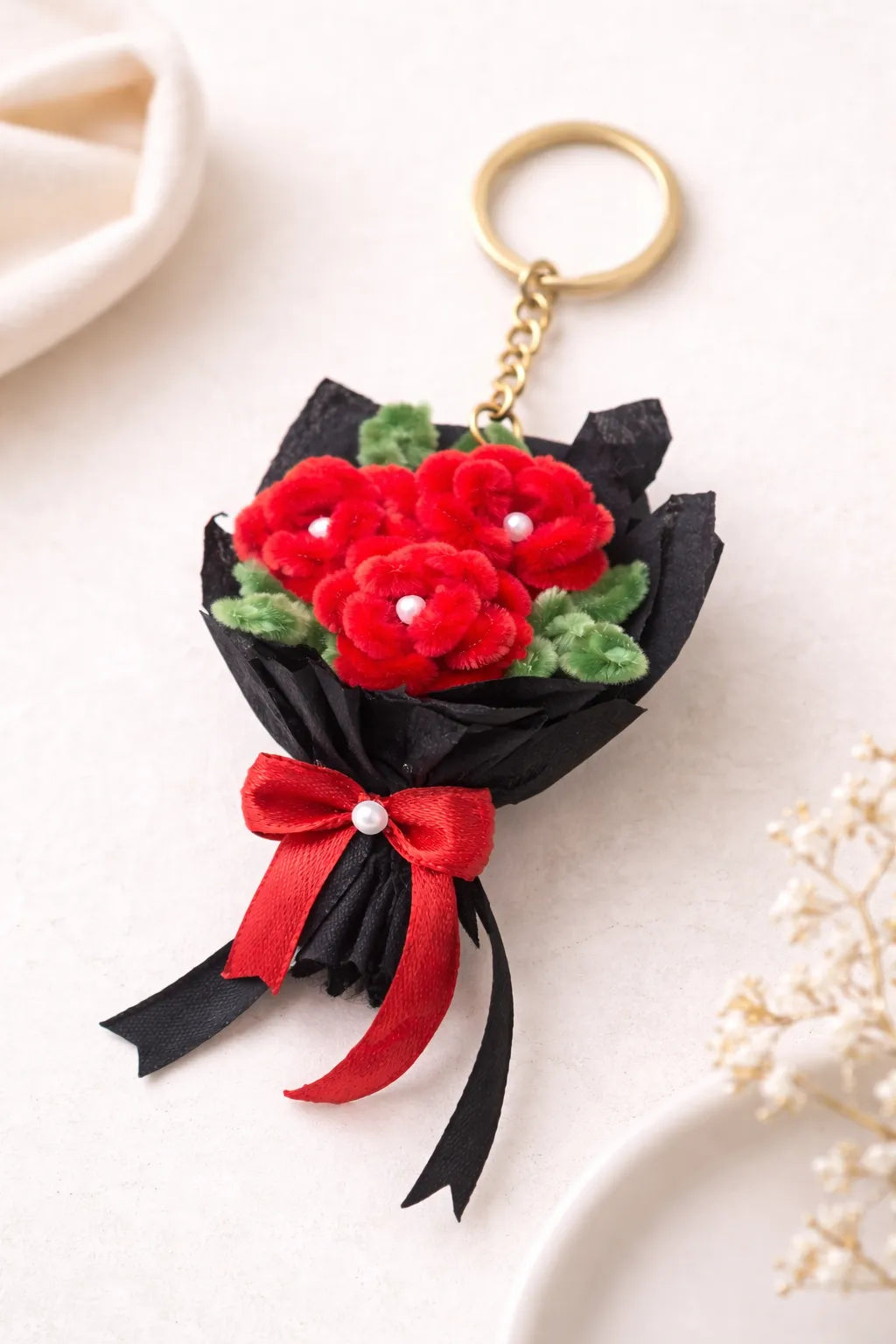 Close-up of handmade pipe cleaner rose bouquet keychain with pearl details, red flowers, green leaves and gold key ring aesthetic product shot