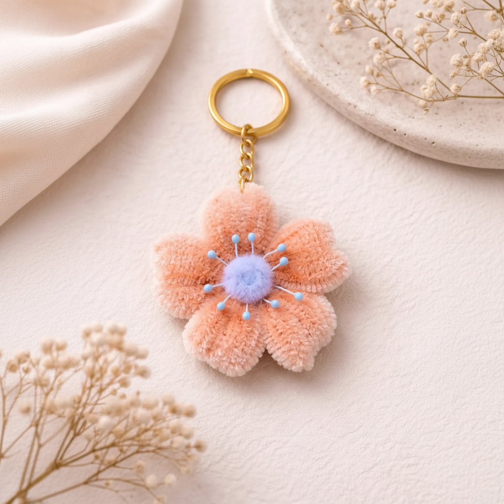 Handmade peach flower keychain with soft plush petals and pastel center attached to gold keyring on neutral aesthetic background
