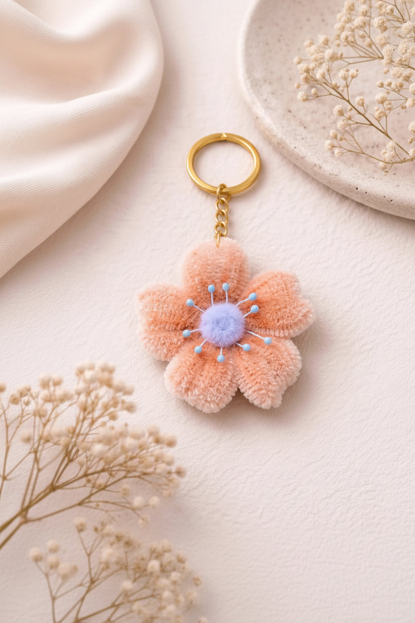 Handmade peach flower keychain with soft plush petals and pastel center attached to gold keyring on neutral aesthetic background